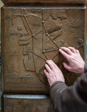Foto Ulf Dahl: Ausschnitt einer Seitenkachel der Stele; tastende Hände auf dem Relief des DB-Netzplans Schleswig-Holstein

