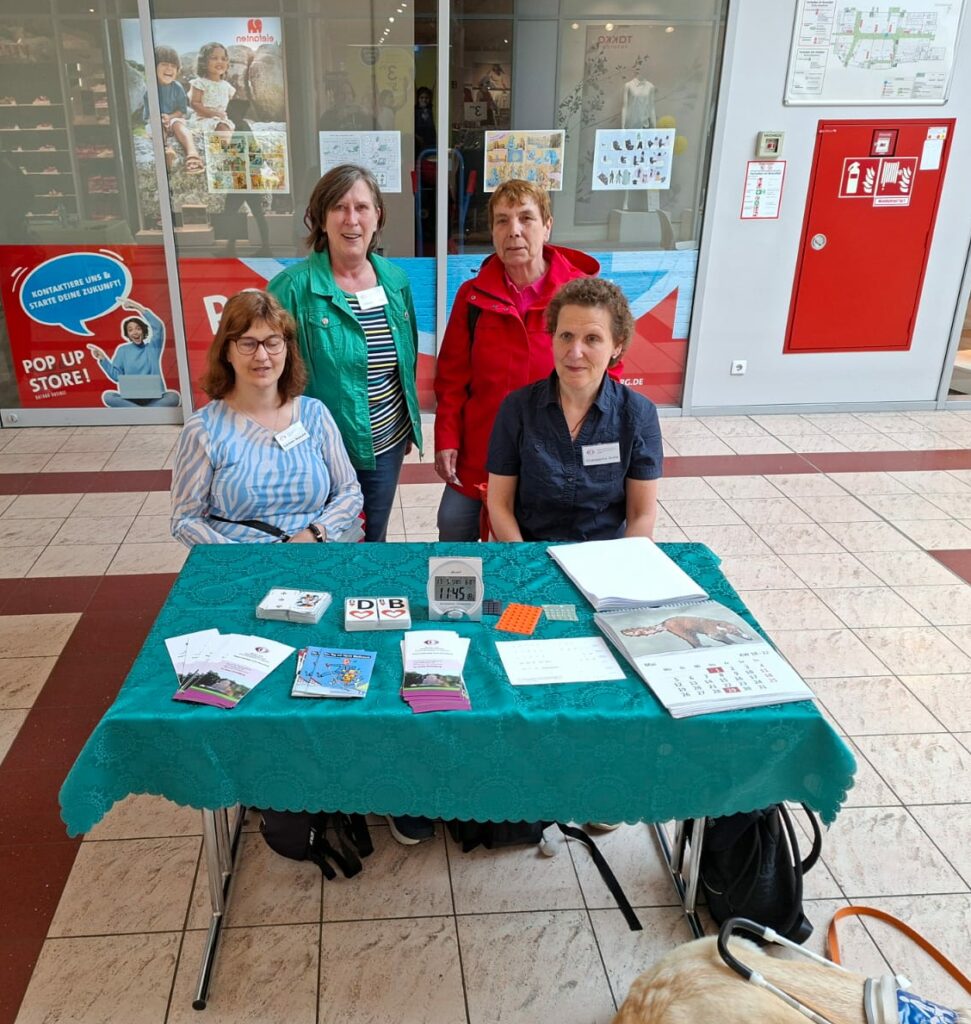 Hinter dem Stand sitzen Carmen Nowald (links), Giuseppina Dolle (rechts), hinter ihnen stehen Petra Heine (links), Kerstin Tomkowitz (rechts),