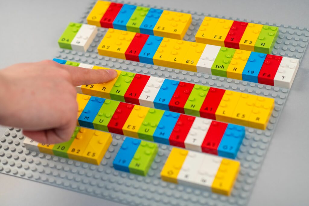 Foto: Niklas Koinzer,
Schrägansicht einer Lego-Platte, auf der ein Veranstaltungshinweis in Braille gelegt ist.