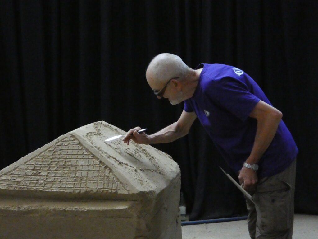 Karl Küppers bearbeitet konzentriert eine hausförmige Sandskulptur mit einem Modellierbesteck.