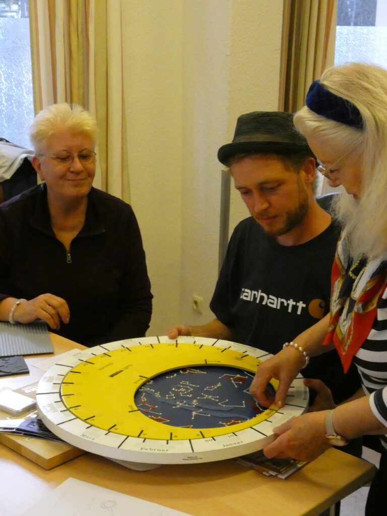 Drei Personen betrachten gemeinsam ein große Himmelsscheibe mit Monats- und Tagesangaben. Die Sternzeichen und Markierungen sind tastbar.