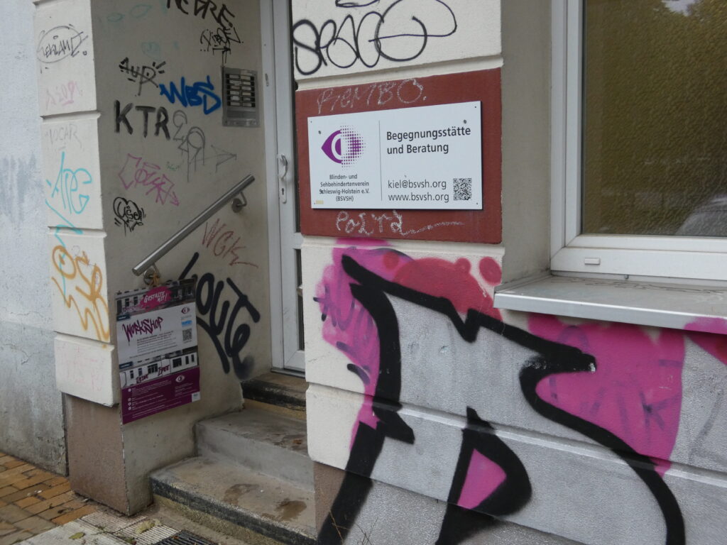 Eingang zur Begegnungsstätte mit beschmierter Fassade und mit Hinweisschild zum Workshop.