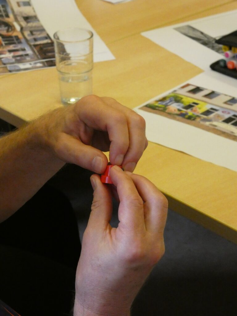 Nahaufnahme von Händen, die ein kleine rote Kunststoffkappe für eine Spraydose ertasten.